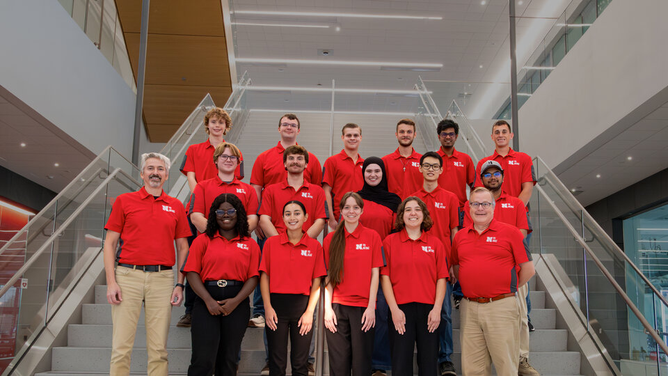 Group of individuals wearing red shirts standing on a staircase in a modern building.